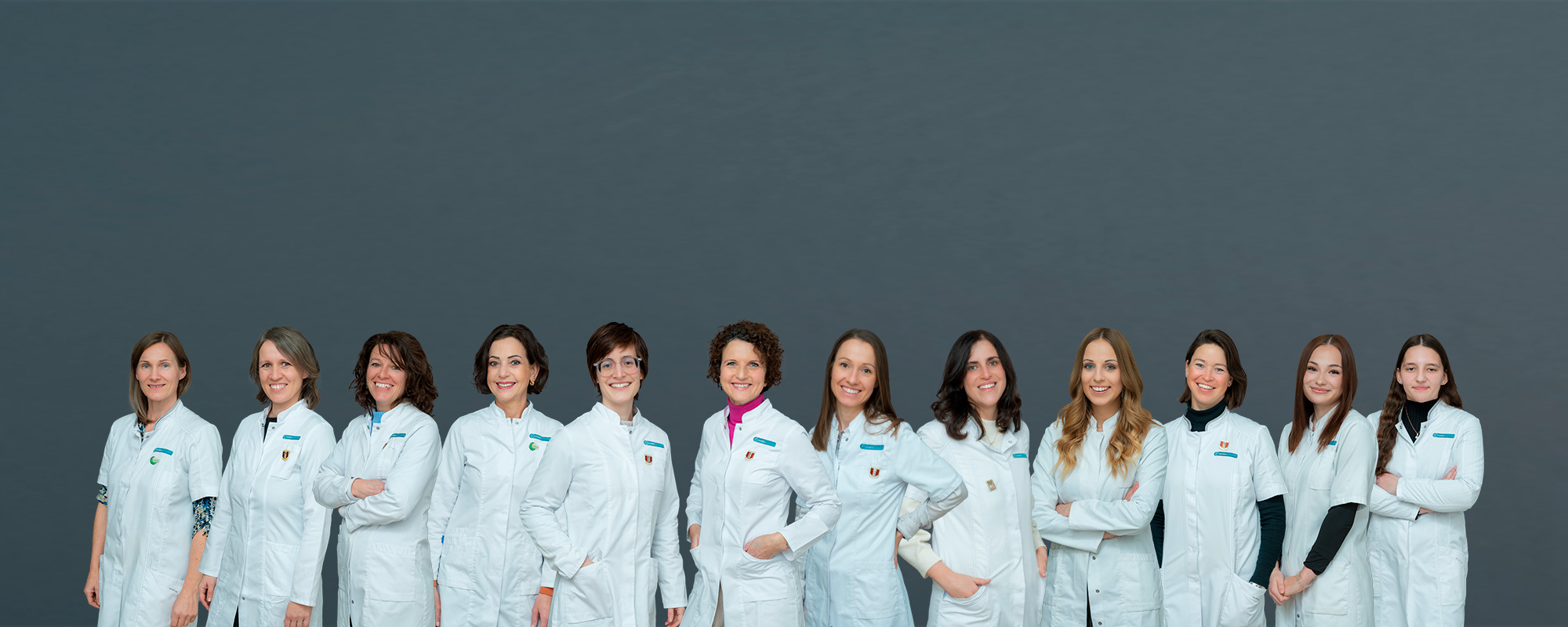 Gruppenfoto von 13 Apothekenmitarbeiterinnen im weißen Kittel vor grauem Hintergrund – professionell und einheitlich inszeniert.